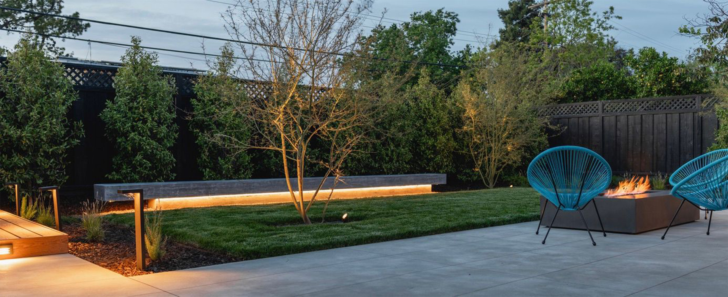 One of our landscaping constructio projects including a concrete terrace or patio, fire pit and a modern large wooden fence with a beautiful illumination from below.